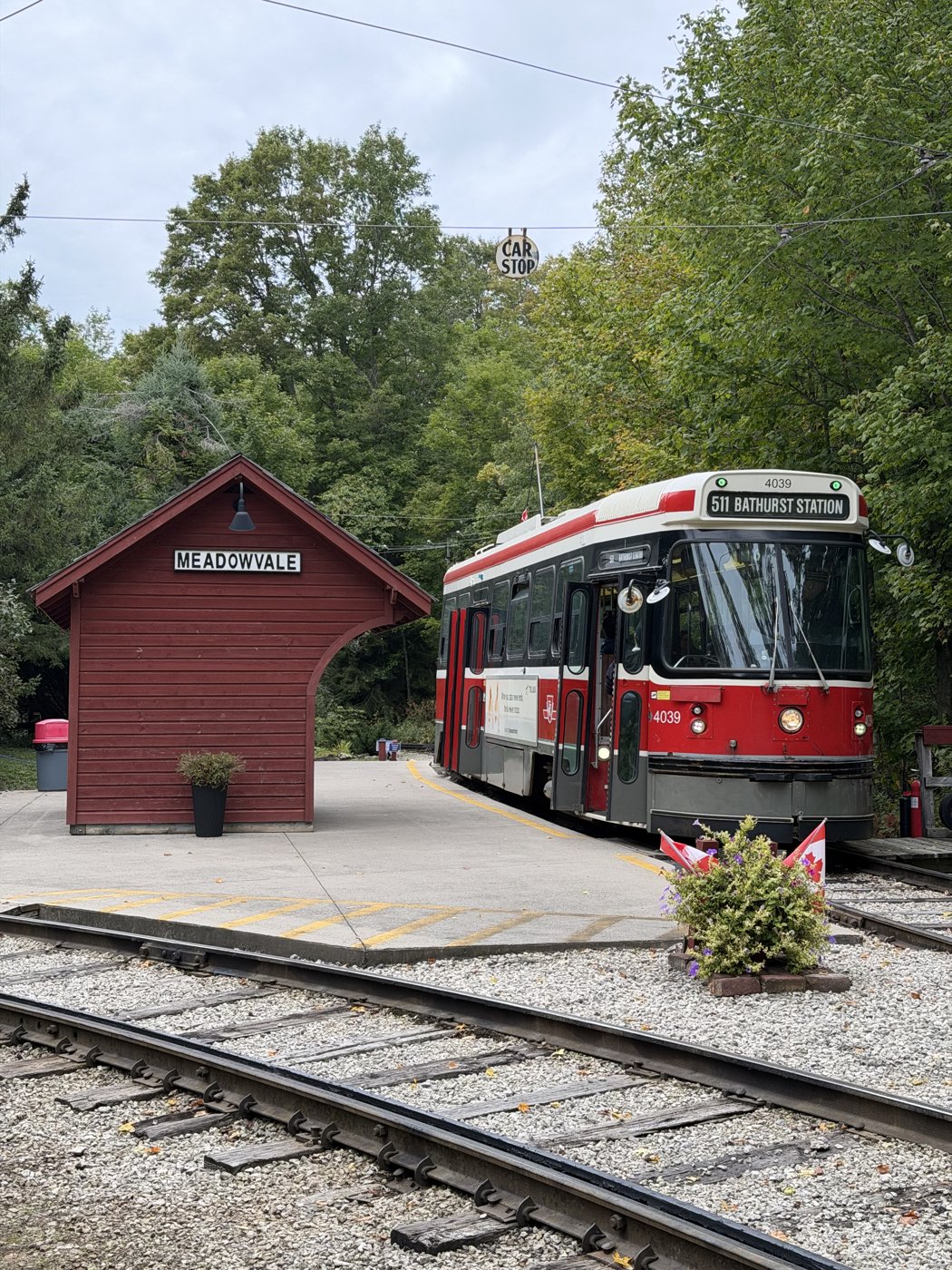 Red and white Halton County Radial Railway streetcar 4039 beside the Meadowvale shelter, with overhead wires and trees.