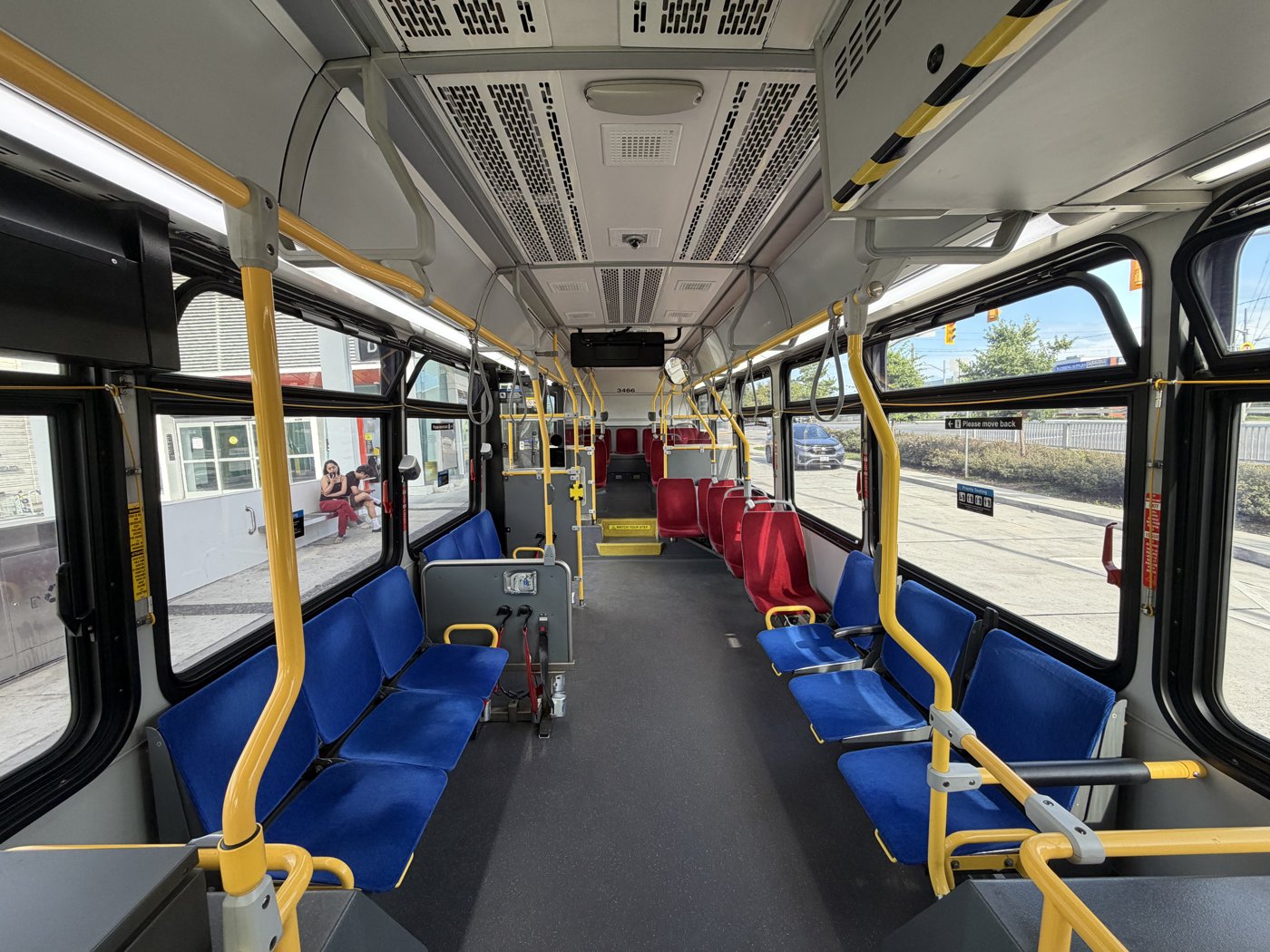 Interior of TTC bus 3466, looking toward the rear past blue and red seats and yellow handrails.
